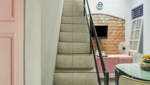 Una escalera conduce a una habitación con pared de ladrillo, un televisor montado en la pared, una mesa con mantel rosa y una silla.