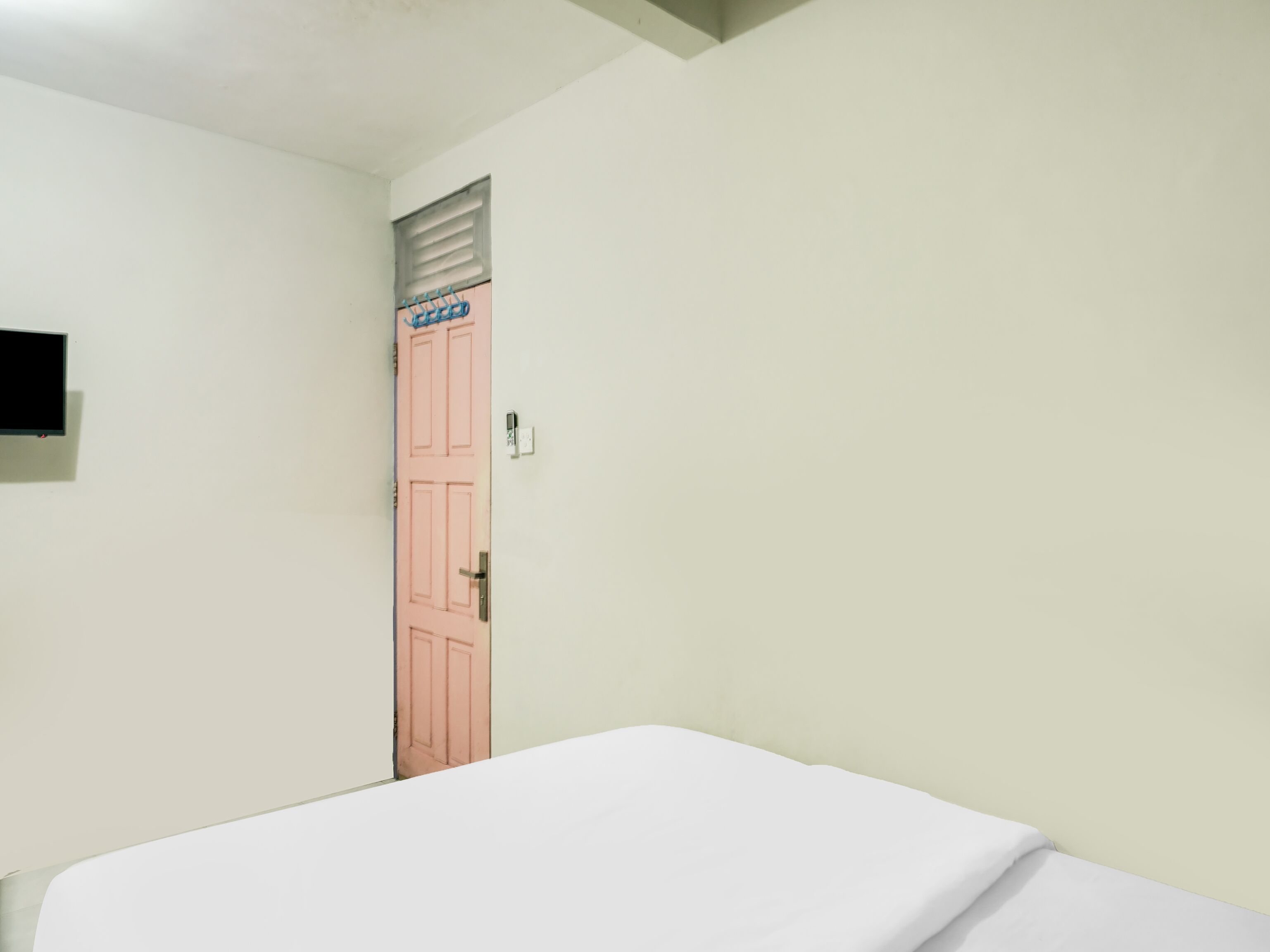 A room with a single bed, a pink door, and a small window with blinds.