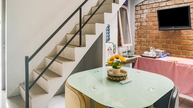 Una sala de estar moderna con una escalera, un televisor de pantalla plana montado en una pared de ladrillo y una mesa redonda de vidrio con un centro decorativo.
