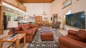 A spacious living room with leather sofas, a dining area, and a kitchen in the background. - Hummingbird Hacienda - Los Ojos Cabin w/ Brazos Cliff Views (Los Ojos)