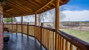 A covered wooden deck with a railing, a hanging swing, and a view of the surrounding landscape. - Hummingbird Hacienda - Los Ojos Cabin w/ Brazos Cliff Views (Los Ojos)