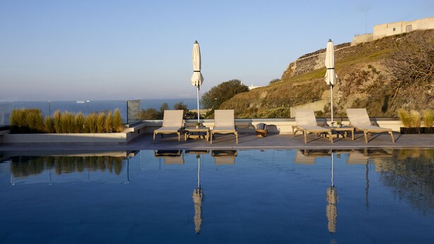Piscina en la azotea con sillas de descanso y sombrillas, con vistas panorámicas a una colina y al mar.