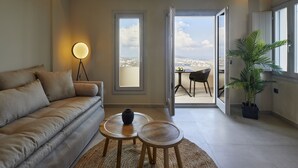 Una sala moderna con un sofá, dos mesas redondas de madera, una lámpara de pie y vistas a un balcón con una mesa y sillas.