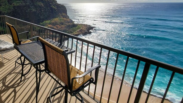 A balcony with two chairs and a table, overlooking a coastal view with a rocky cliff and the ocean.