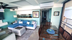 A modern living room with a sectional sofa, a dining table with chairs, and a staircase leading to an upper level.