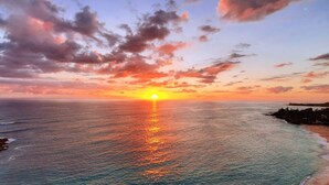 A sunset over the ocean with a beach and rocky coastline.