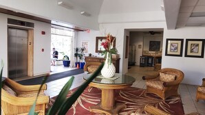 A lobby with wicker furniture, a red patterned carpet, and a ceiling mural of palm trees and clouds.