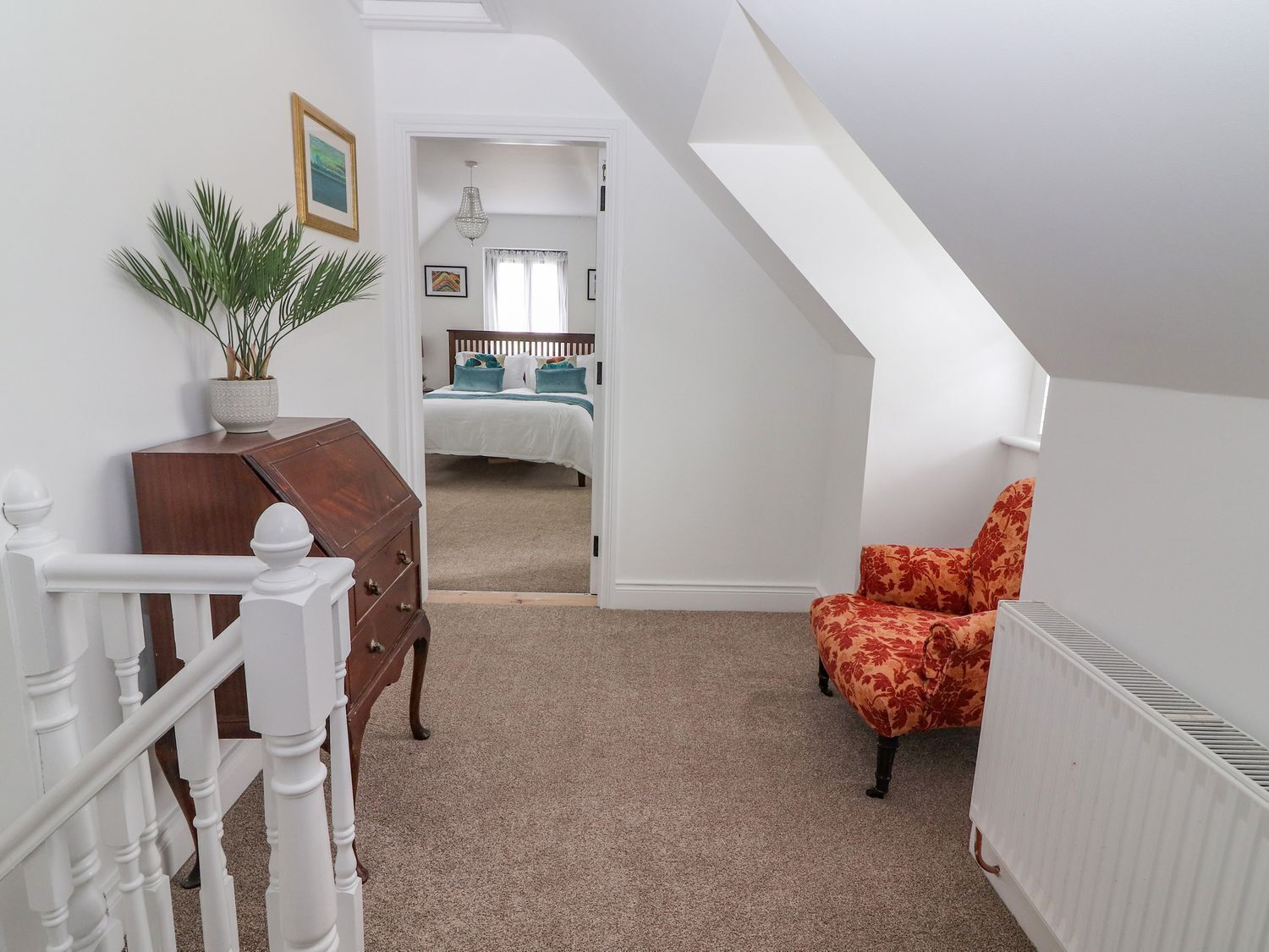 A bedroom with a bed, a dresser, a chair, a radiator, and a potted plant.