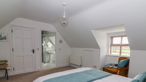 Een slaapkamer met een bed, een stoel, een raam, een radiator en een deur naar een badkamer.