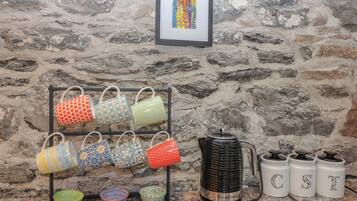 A kitchen with a stone wall, a framed cityscape, a mug rack, a kettle, and labeled storage containers.