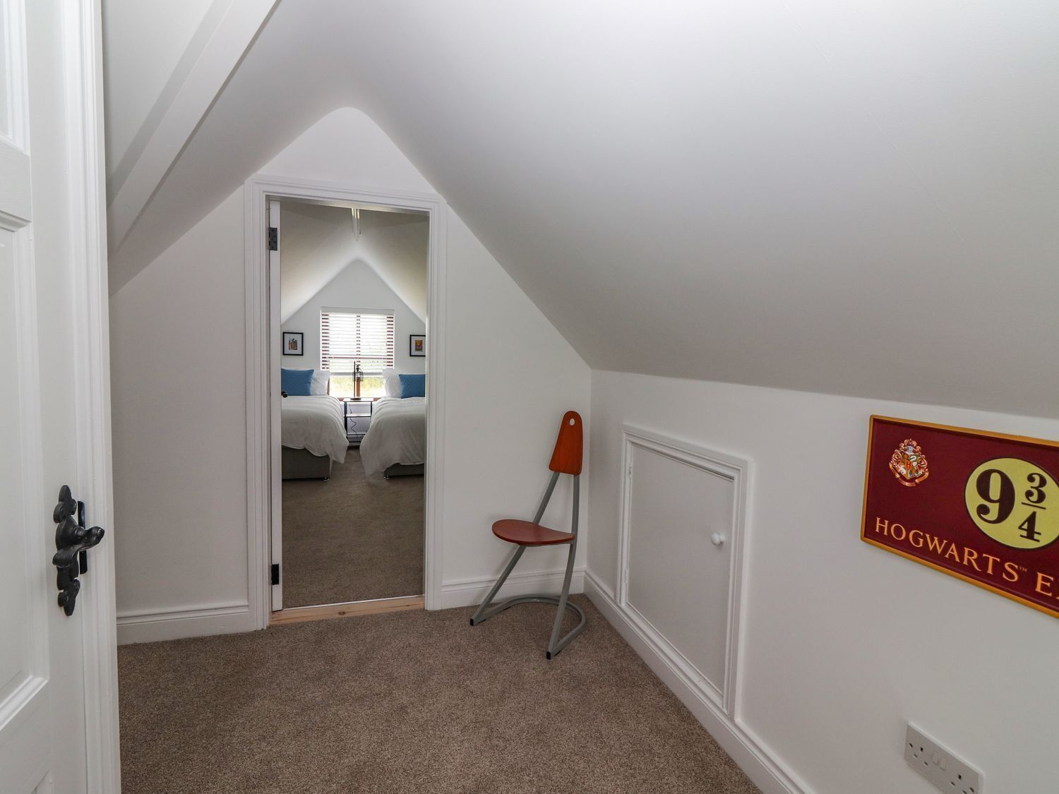 A bedroom with two beds, a chair, a coat rack, and a Hogwarts sign on the wall.
