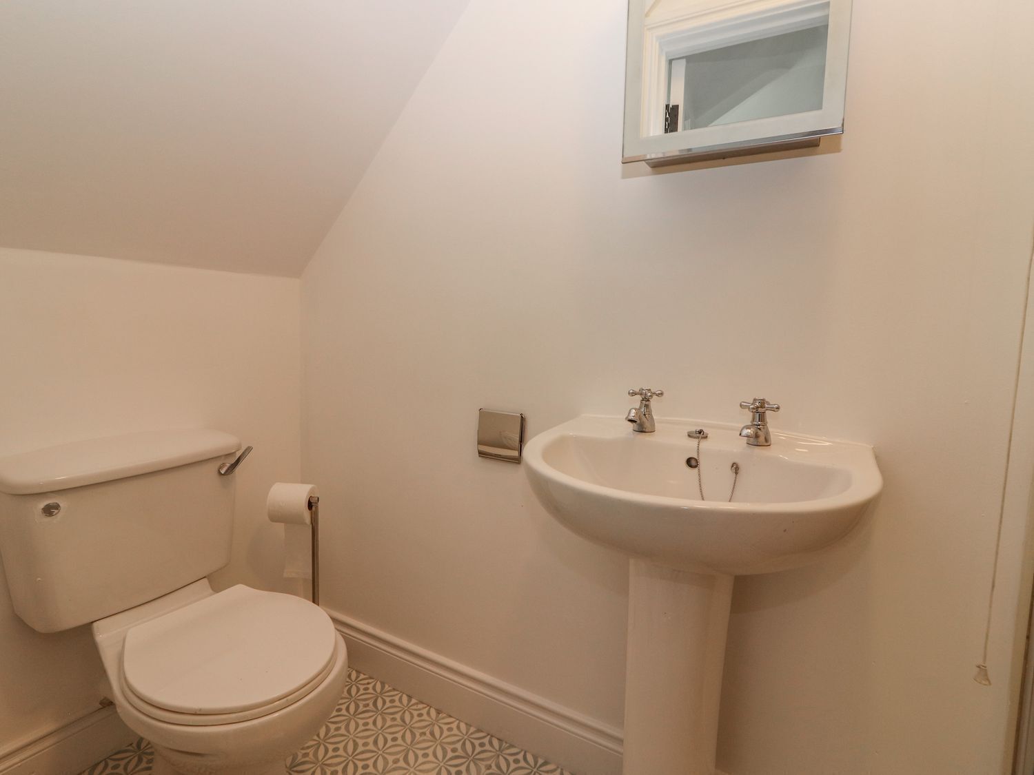 Une petite salle de bain blanche, avec des toilettes, un lavabo et une fenêtre située au-dessus du lavabo.