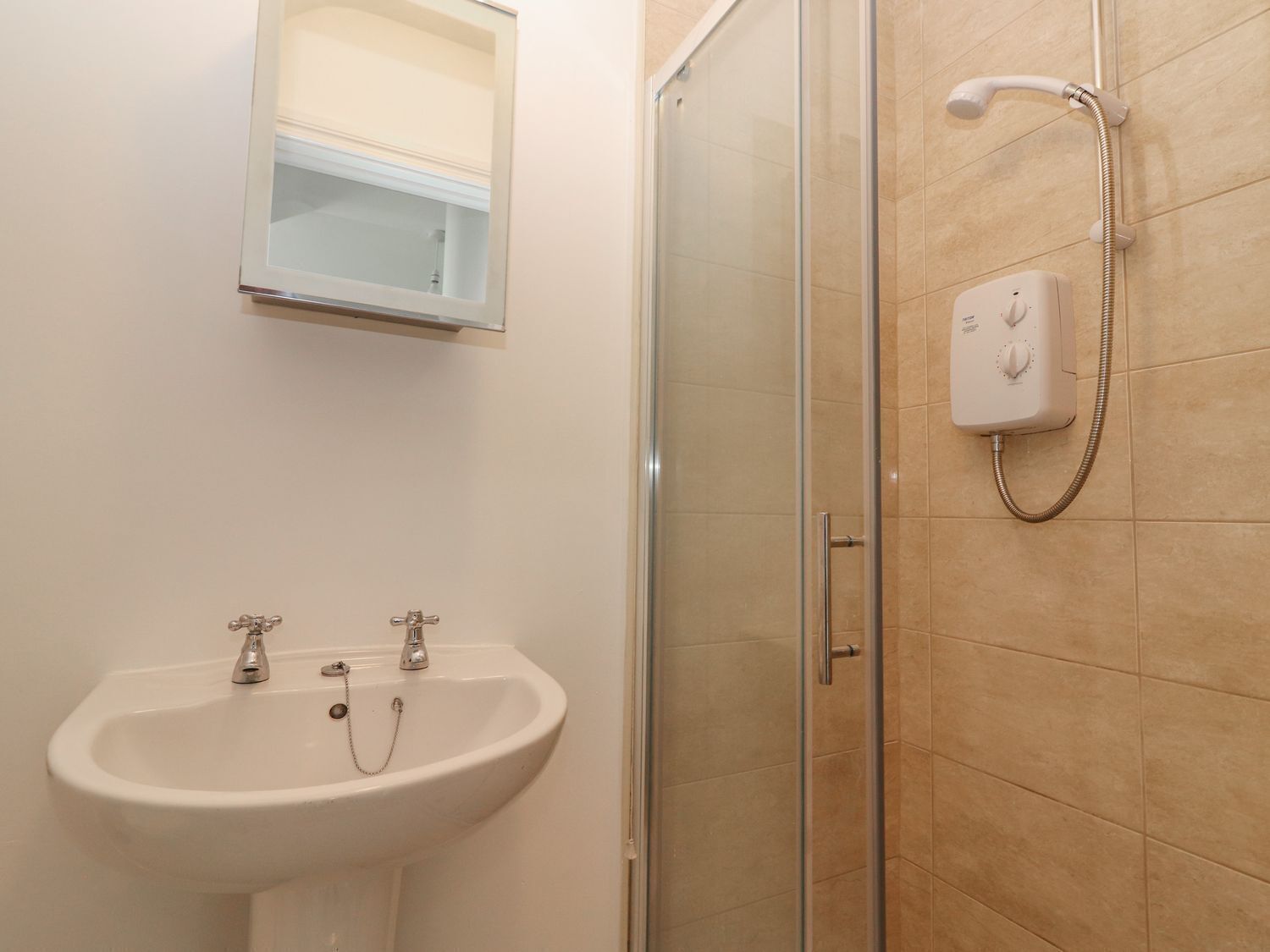 A bathroom with a glass-enclosed shower, a sink with two faucets, and a wall-mounted mirror.