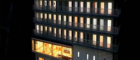 Un hotel de varios pisos con ventanas y balcones iluminados, con un letrero en idioma extranjero.
