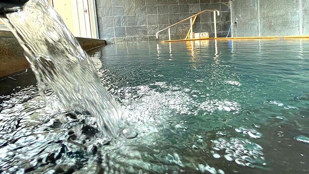 A clear indoor pool with a water fountain feature, surrounded by dark stone walls and a wooden ceiling. - Jisco Hotel Obama Onsen (Unzen)