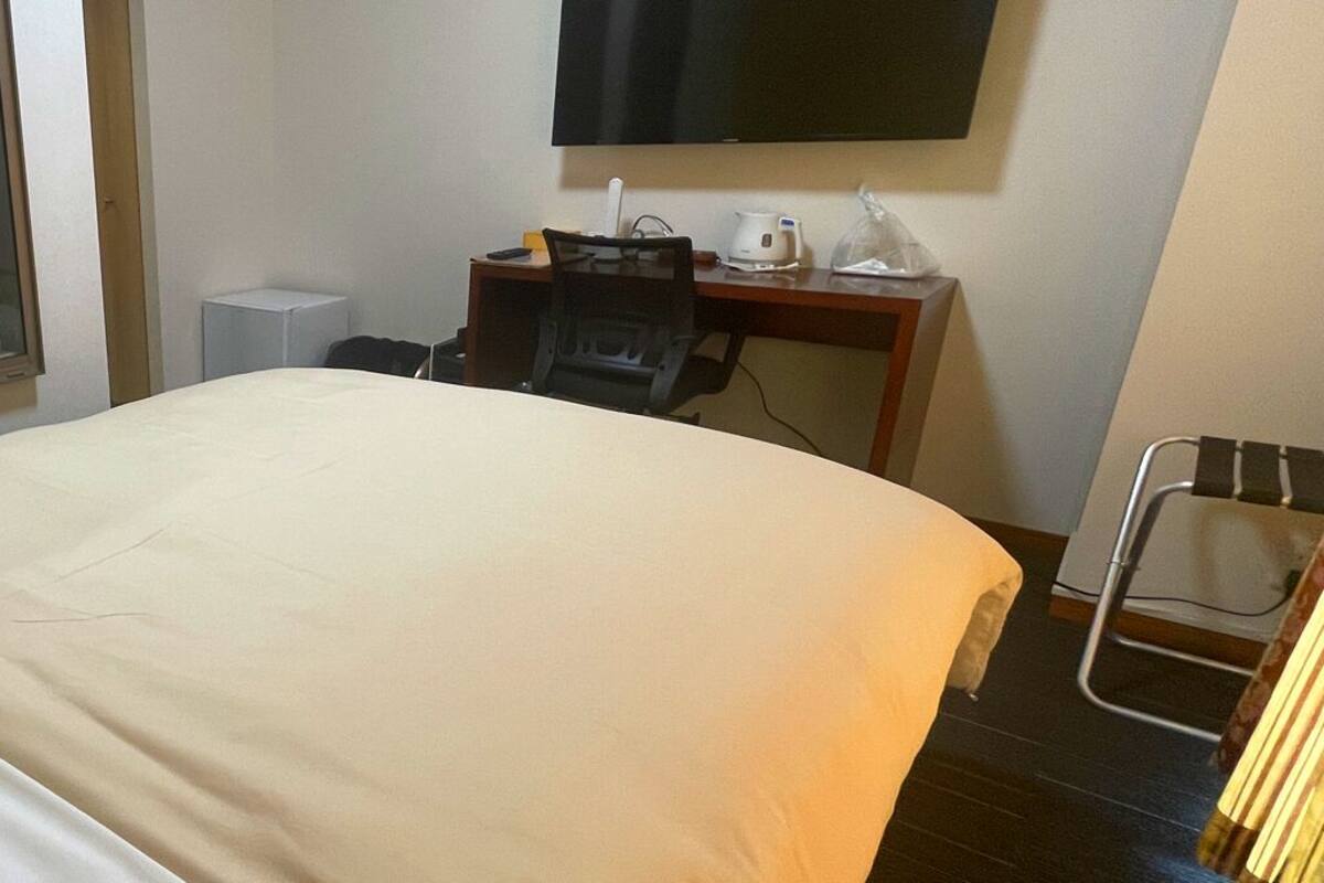 A hotel room with a bed, a desk, a chair, a TV, and a window with curtains.