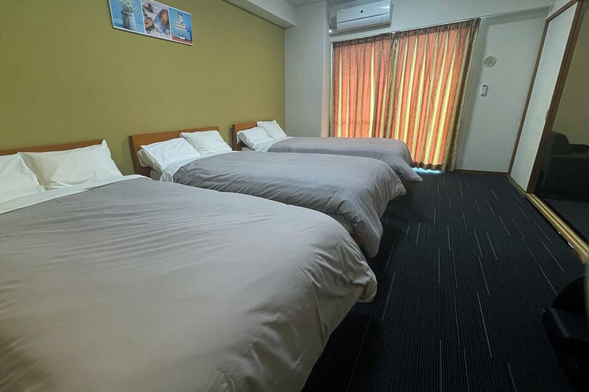 A hotel room with three beds, a large mirror, and a window with curtains.