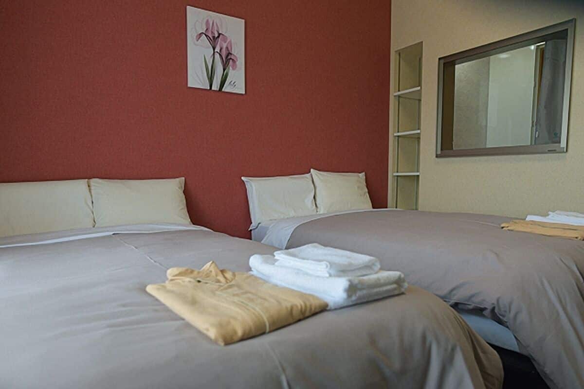 A hotel room with two beds, beige walls, a painting of flowers, and a window.