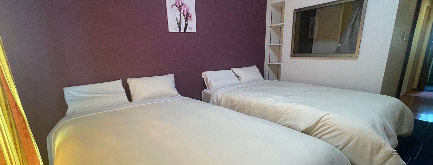 Una habitación con dos camas, una pared morada y una ventana.