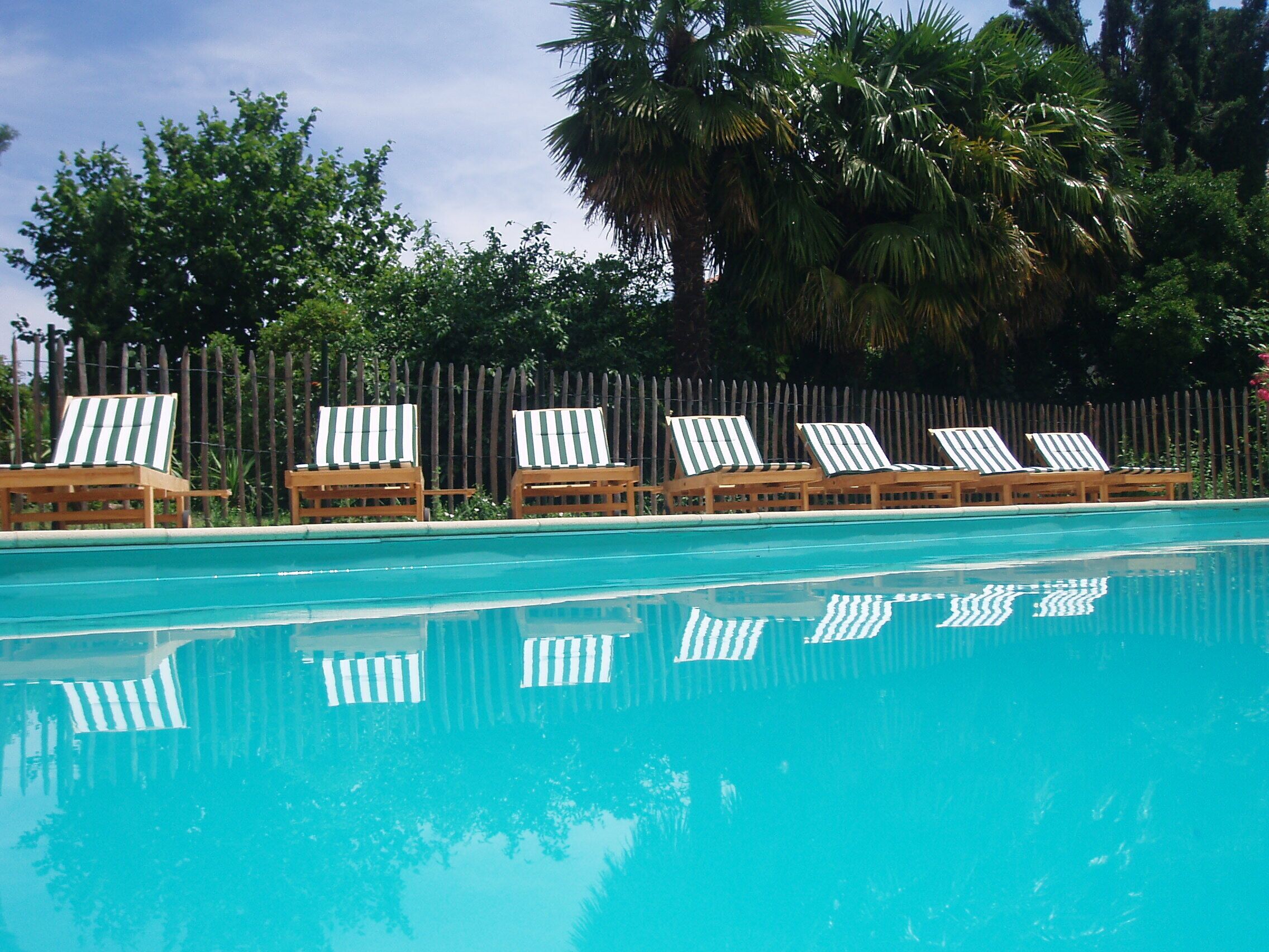 A swimming pool with six lounge chairs and a wooden fence.