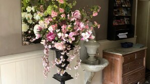 A room with a floral arrangement on a pedestal, a mirror on the wall, a bookshelf, and a patterned floor. - La Cerisaie (Riols)