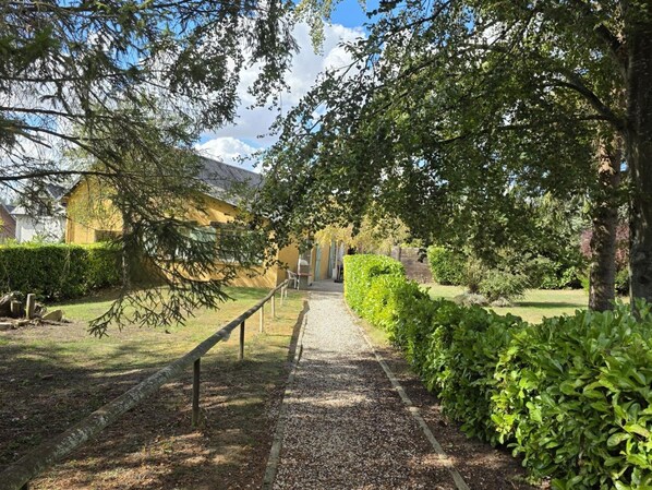 A gravel pathway leading to a building with a yellow facade, surrounded by greenery and trees.