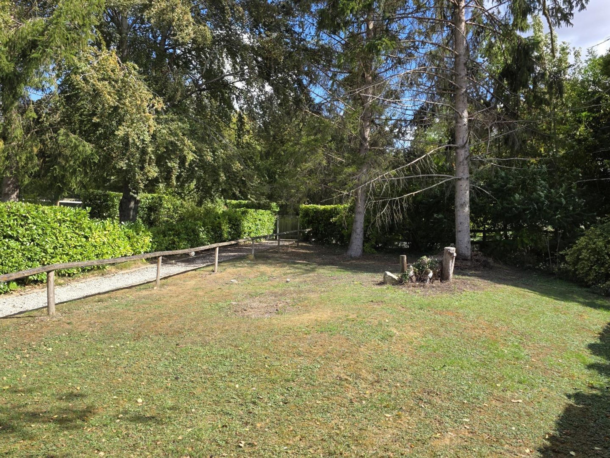 Un espacio exterior cercado con un sendero de grava, rodeado de abundante vegetación y árboles.