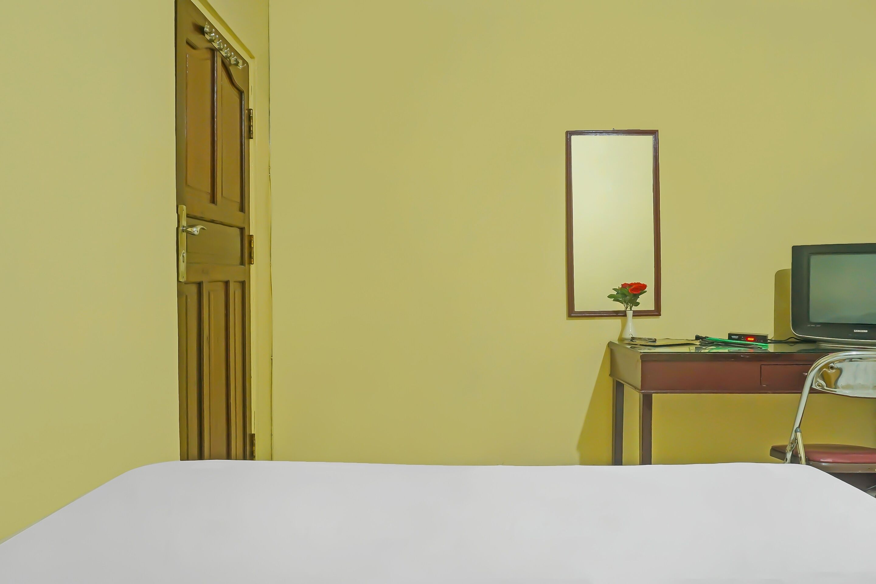 Ein Hotelzimmer mit Bett, Schreibtisch, Computer, Stuhl und Tür.