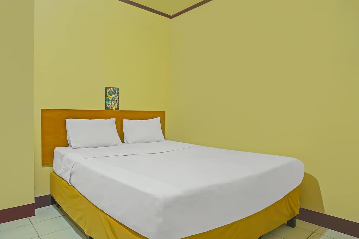 A bed with a wooden headboard, white bedding, and a small decorative item on the wall.