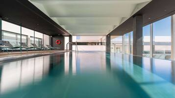 Ein moderner, überdachter Pool mit Panoramafenstern, einer großzügigen Liegefläche und Blick auf die Stadtlandschaft.