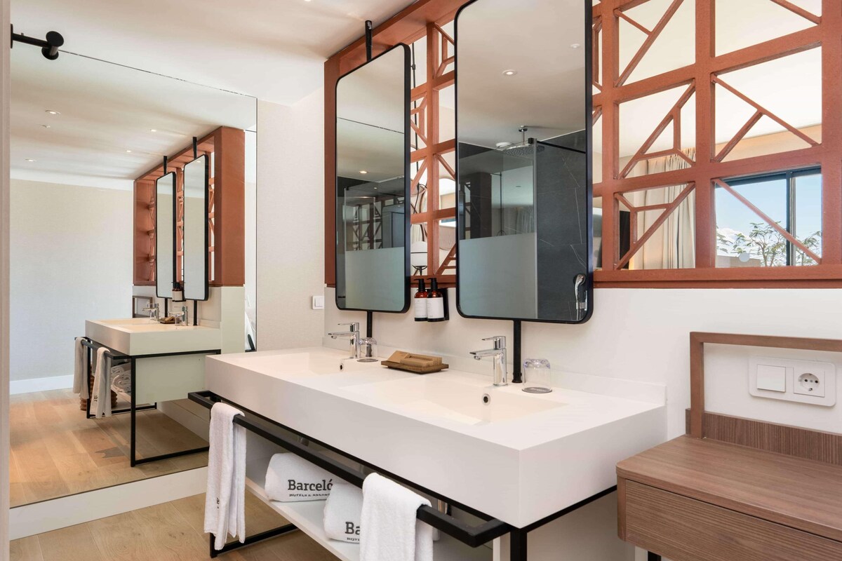 A hotel bathroom with a large mirror, two sinks, and a wooden vanity.