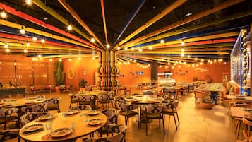 A spacious restaurant with multiple dining tables and chairs, a cactus decoration, and a variety of hanging lights.