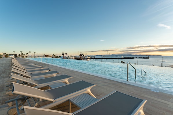 Una piscina al aire libre, sombrillas, sillones reclinables de piscina