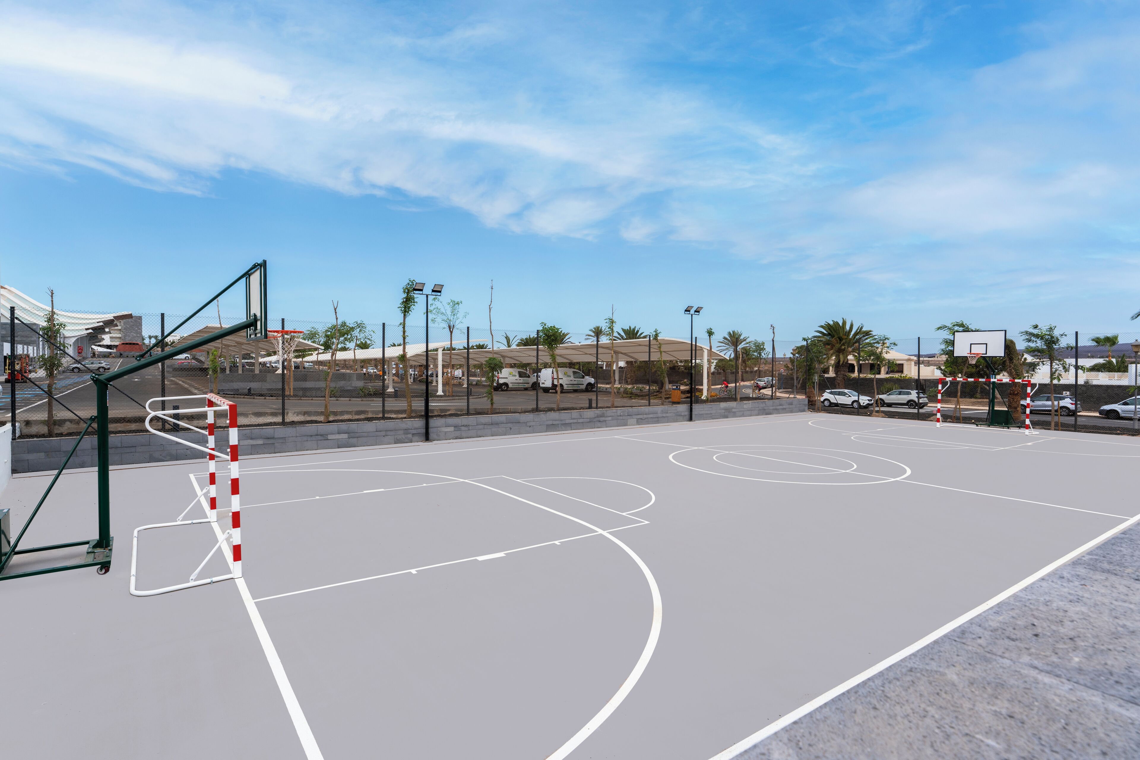 Ein Basketballplatz im Freien mit Korb, umgeben von einem Zaun und Palmen.