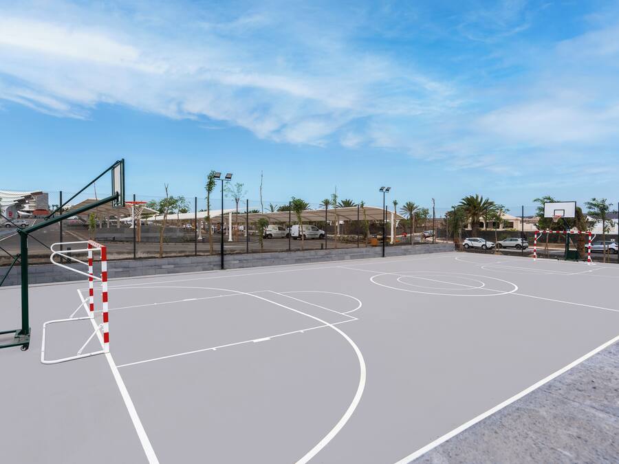 Ein Basketballplatz im Freien mit Korb, umgeben von einem Zaun und Palmen.