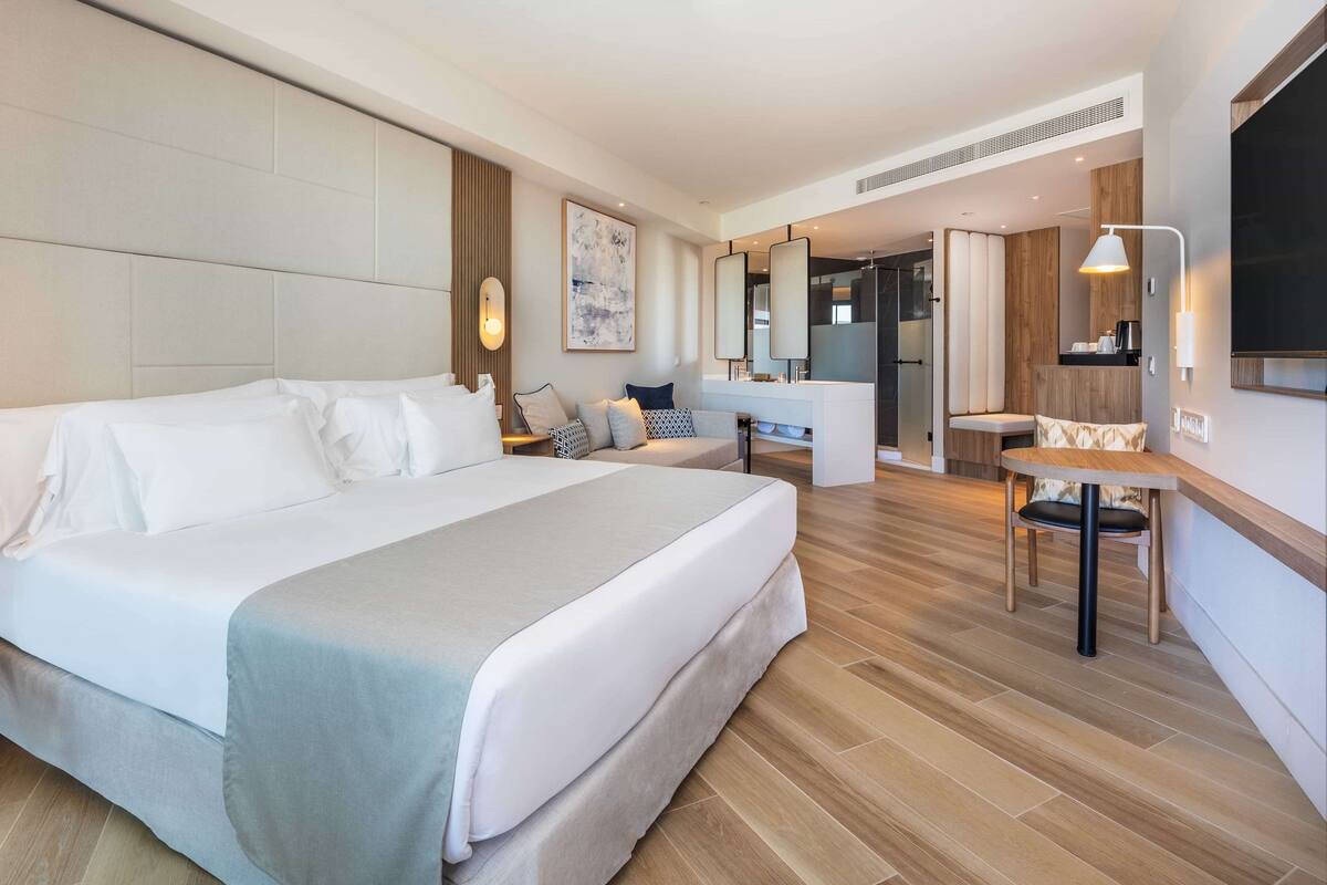 A modern hotel room with a large bed, a desk, a chair, and a TV.