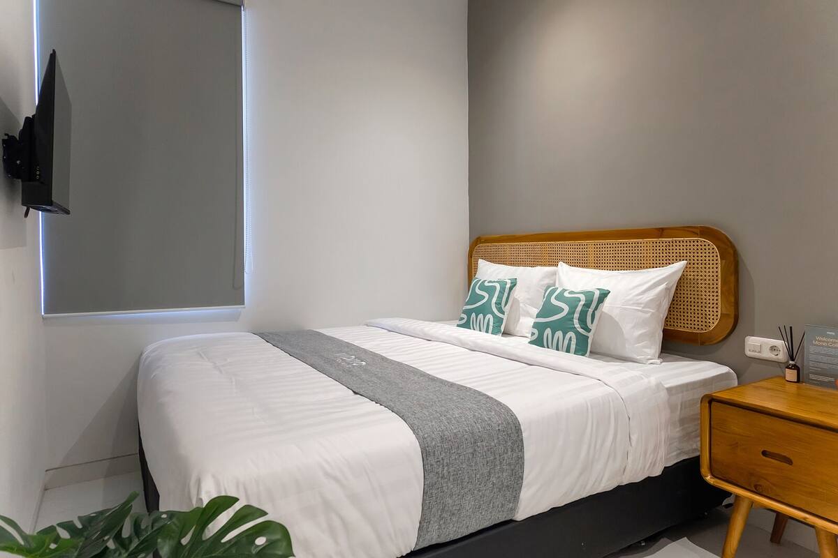 A modern bedroom with a bed, a bedside table, a wall-mounted TV, and a window.