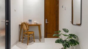 A small, clean room with a wooden door, a desk with a chair, a potted plant, and a mirror on the wall. - Mono Coliving Pakis, Surabaya (Surabaya)
