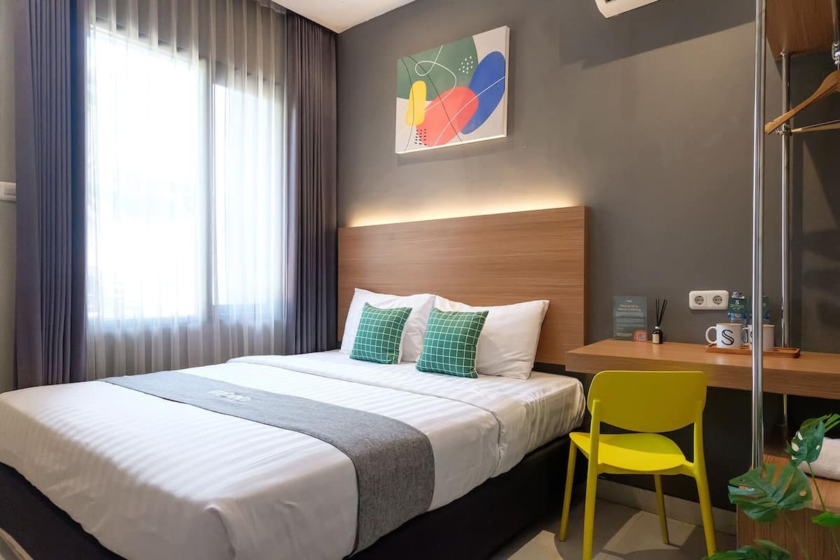 A hotel room with a bed, a desk, a chair, and a window with curtains.