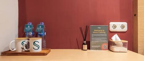 A reception area with a wooden table displaying branded mugs, a welcome sign, a water dispenser, and a tissue box.