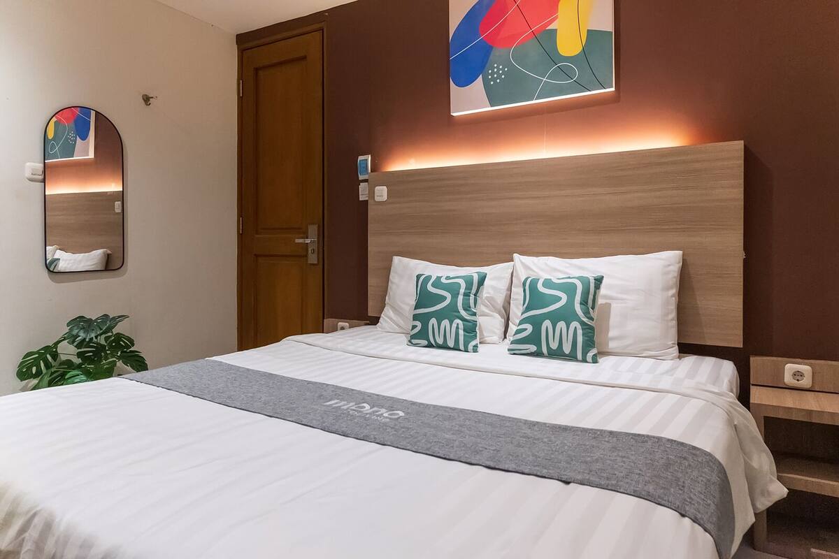 A hotel room with a large bed, a wooden headboard, a mirror, and a wall art piece.