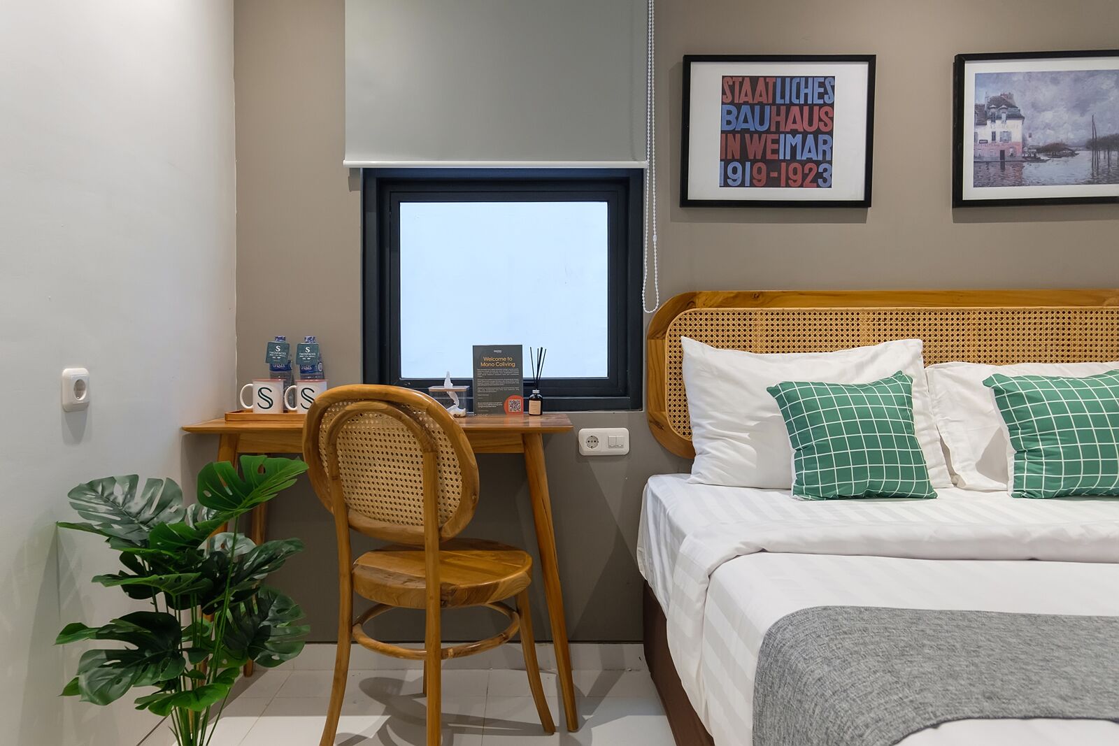 Une chambre d’hôtel avec un bureau en bois, une chaise, un lit avec des oreillers verts et deux tableaux encadrés au mur.