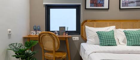 Une chambre d’hôtel avec un bureau en bois, une chaise, un lit avec des oreillers verts et deux tableaux encadrés au mur.