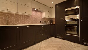 A modern kitchen with dark cabinetry, a herringbone-patterned floor, and a built-in oven. - Bellerose 6 (Lancaster)
