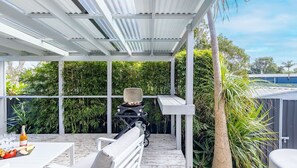 Un patio abrité avec un barbecue, un coin salon et une végétation luxuriante.