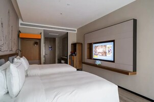 A hotel room with two beds, a TV mounted on the wall, and a wooden cabinet.