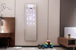 A modern room with a wall-mounted digital display showing exercise icons, a wooden side table with a water bottle, and a white couch.