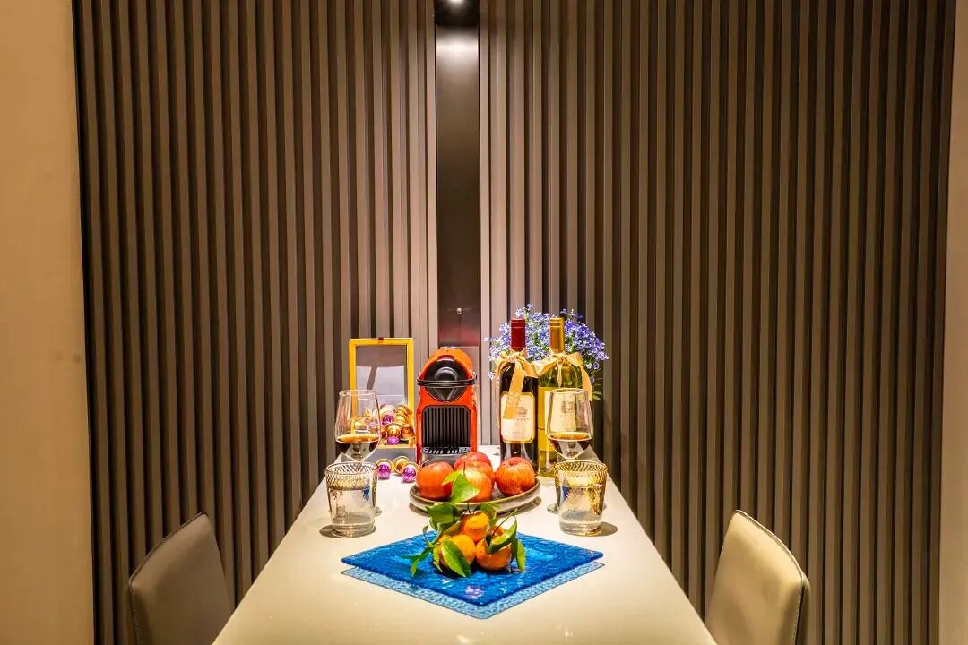 Una mesa de comedor dispuesta con arreglos de frutas, dos botellas de vino y un adorno.