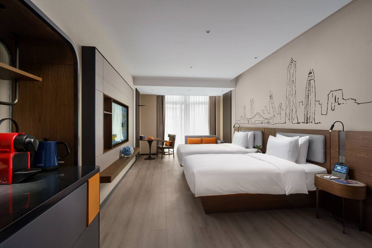 A hotel room with two beds, a kitchenette, a dining area, and a cityscape mural on the wall.