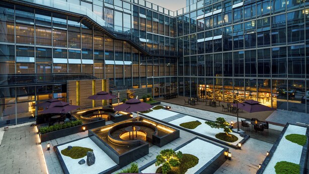 Un edificio moderno con fachada de vidrio, espacios de estar al aire libre y un patio ajardinado.
